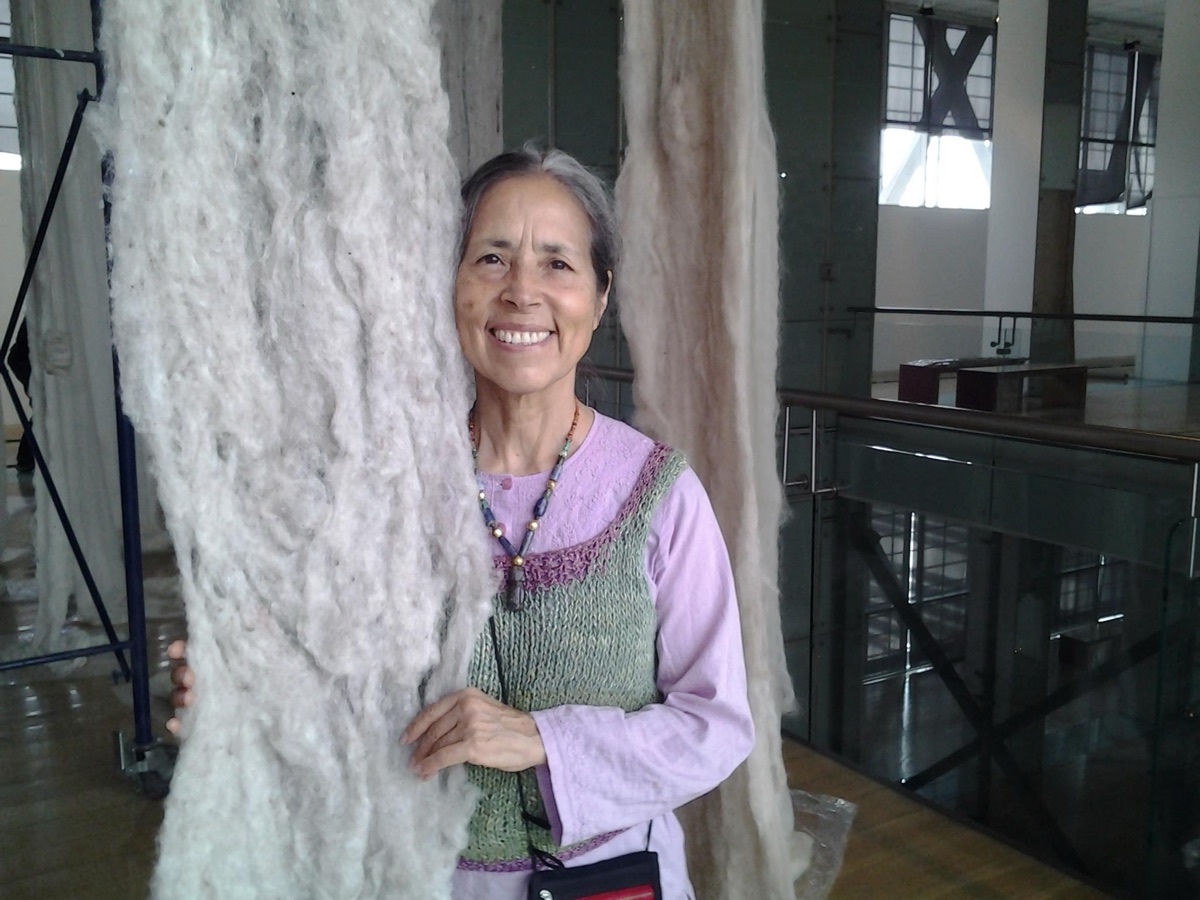 Cecilia Vicuña standing beside a hanging fiber work at Museo Nacional de Bellas Artes in Chile