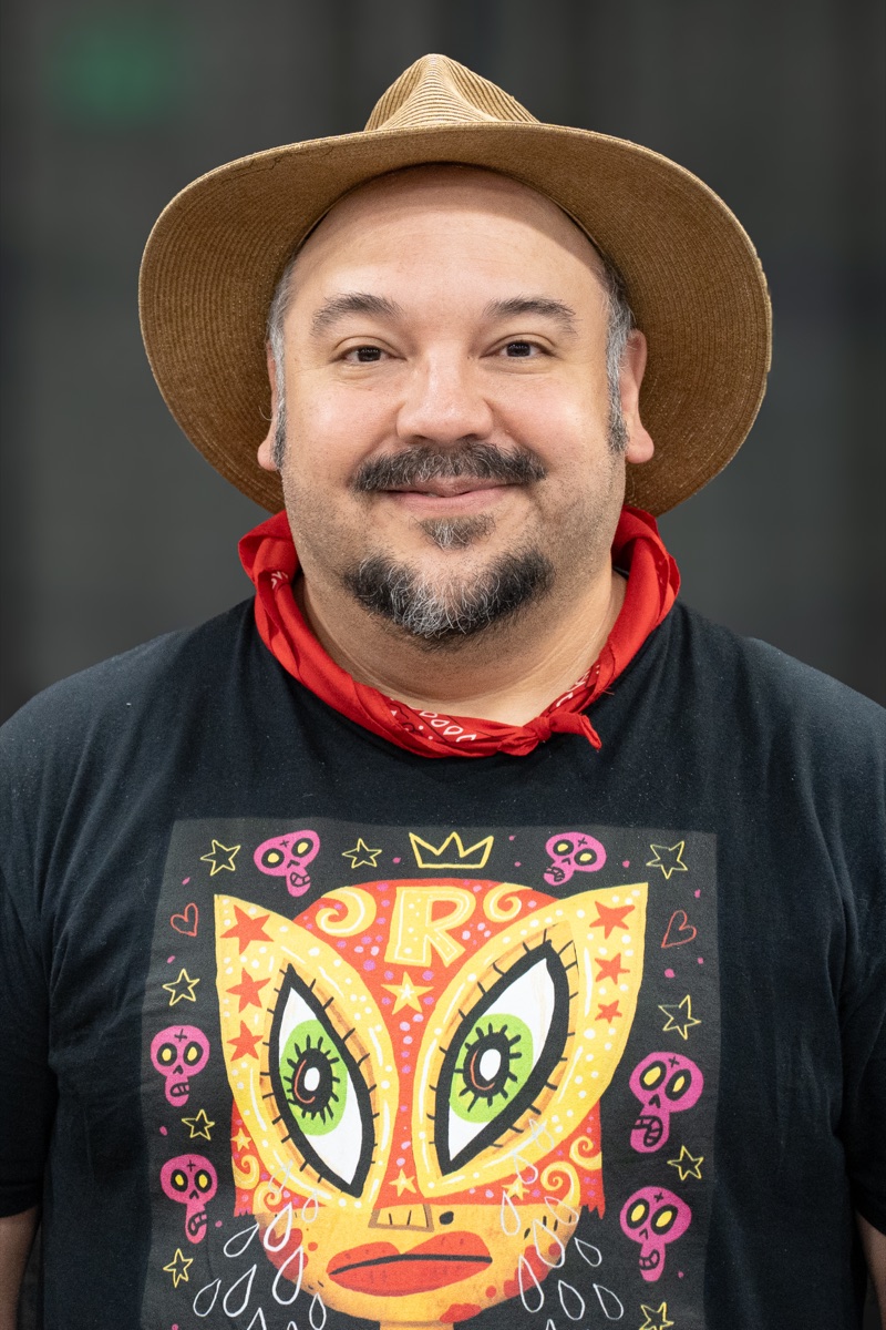 Jorge R. Gutiérrez wearing a hat, red bandanna, and colorful T-shirt at Comic Con Oakland in 2026
