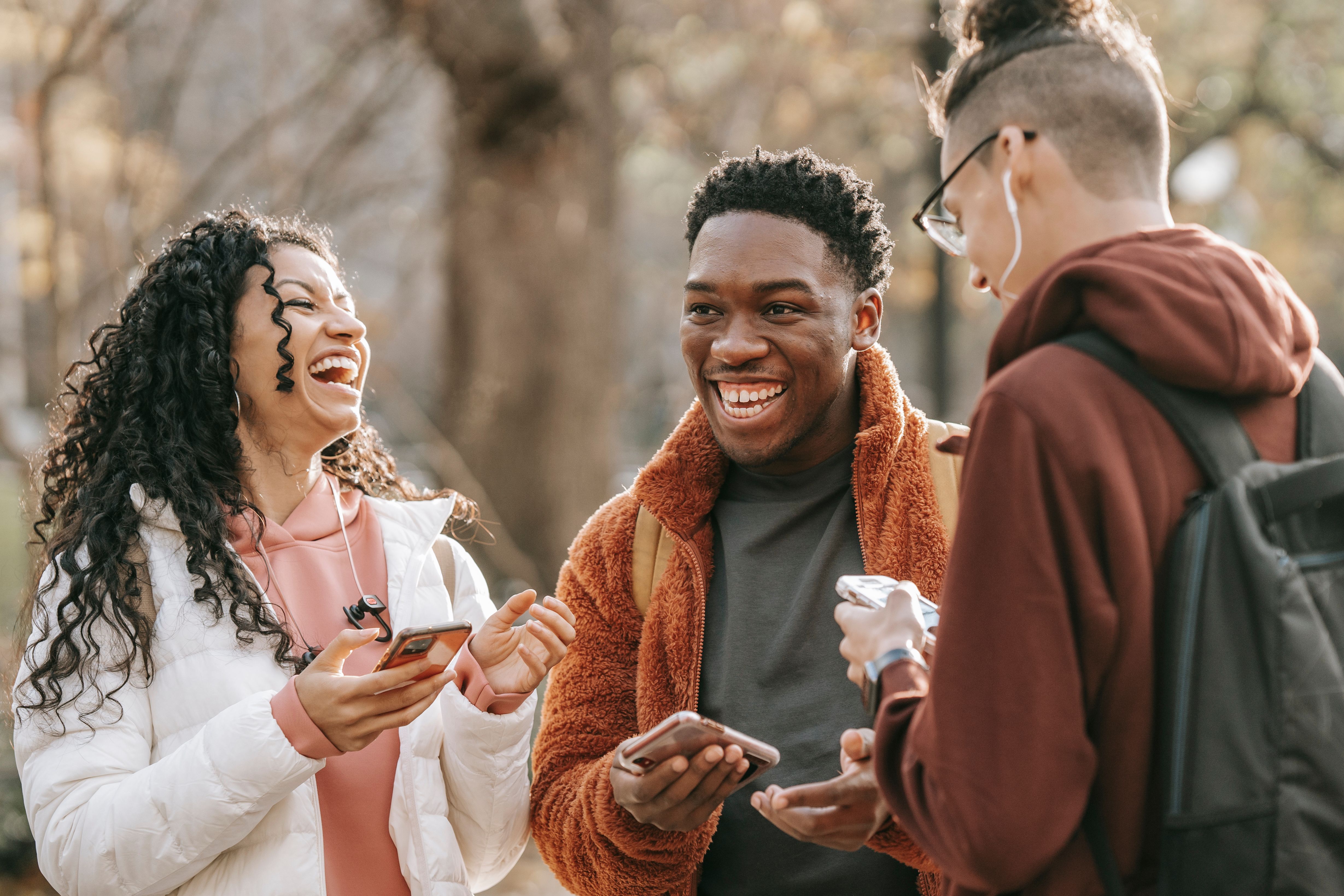 Three people sharing a smiling conversation outdoors, with phones in hand.